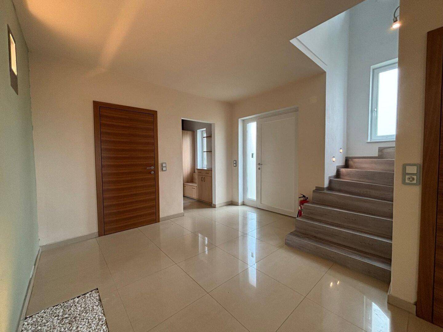 Heller Flur mit Fliesenboden, Holztüren und Zugang zu den oberen Etagen über eine Treppe.