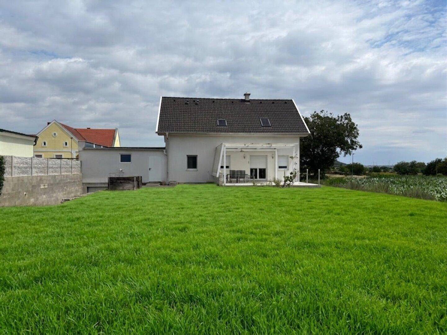 Gepflegter Garten mit weitläufigem Rasen und überdachter Terrasse am hinteren Teil des Hauses.