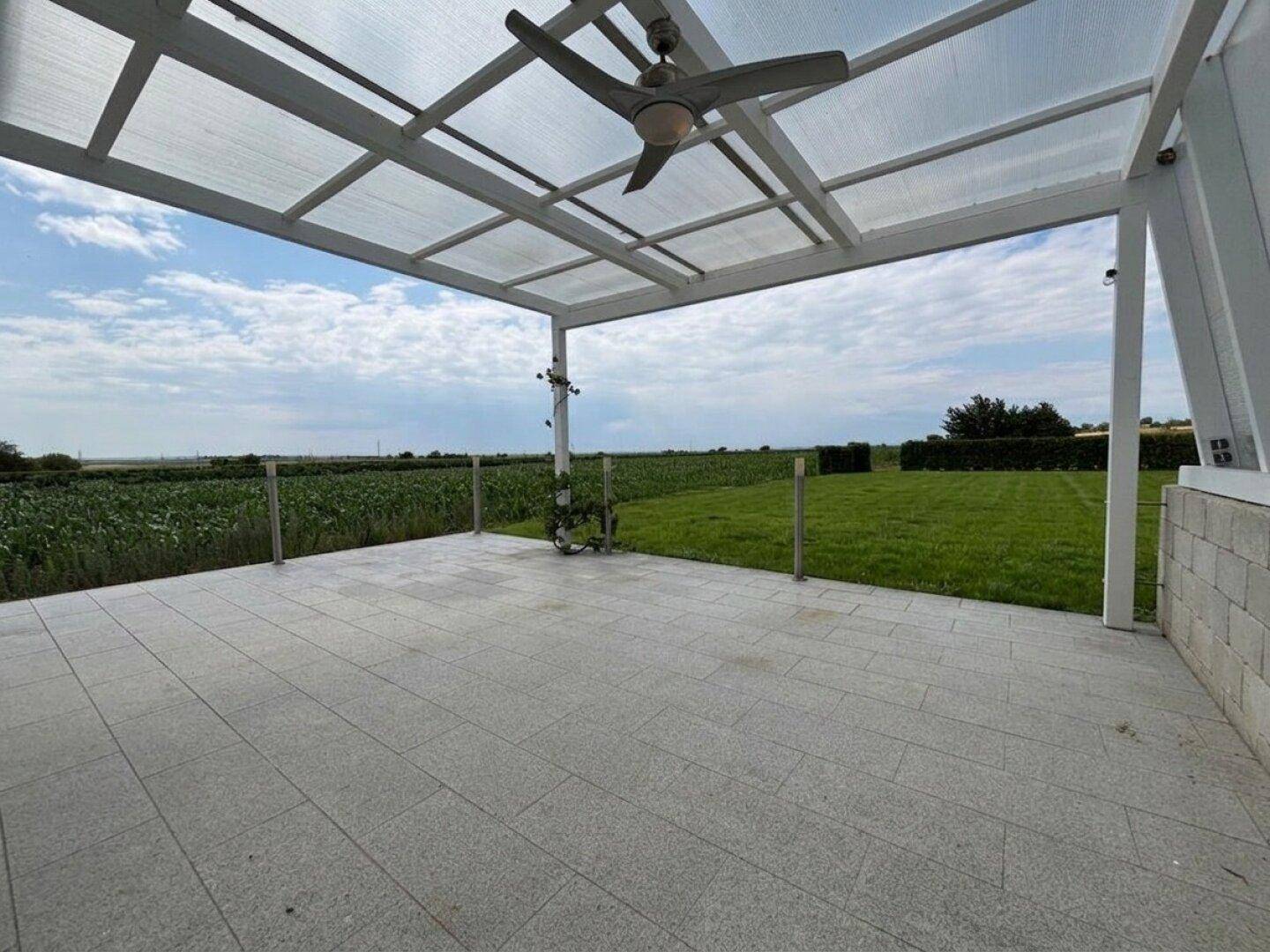 Geräumige, überdachte Terrasse mit Fliesenboden und unverbautem Blick auf die Felder.