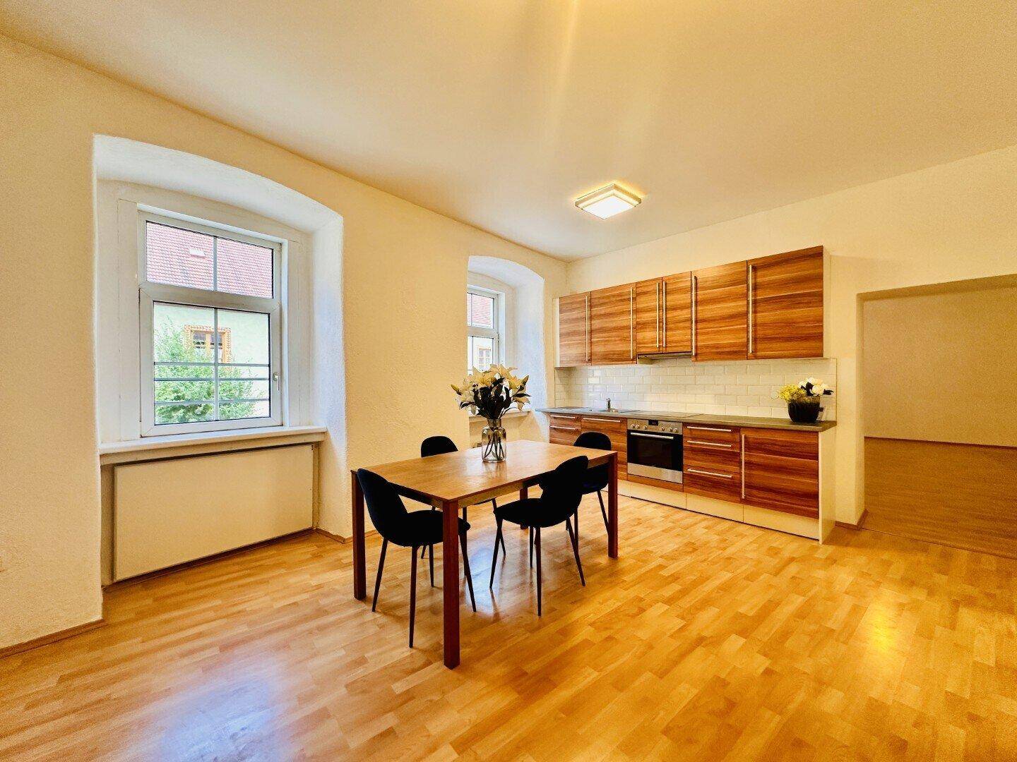 Geräumige Wohnküche mit Holzboden, modernen Holzschränken, Essbereich und Fenstern.