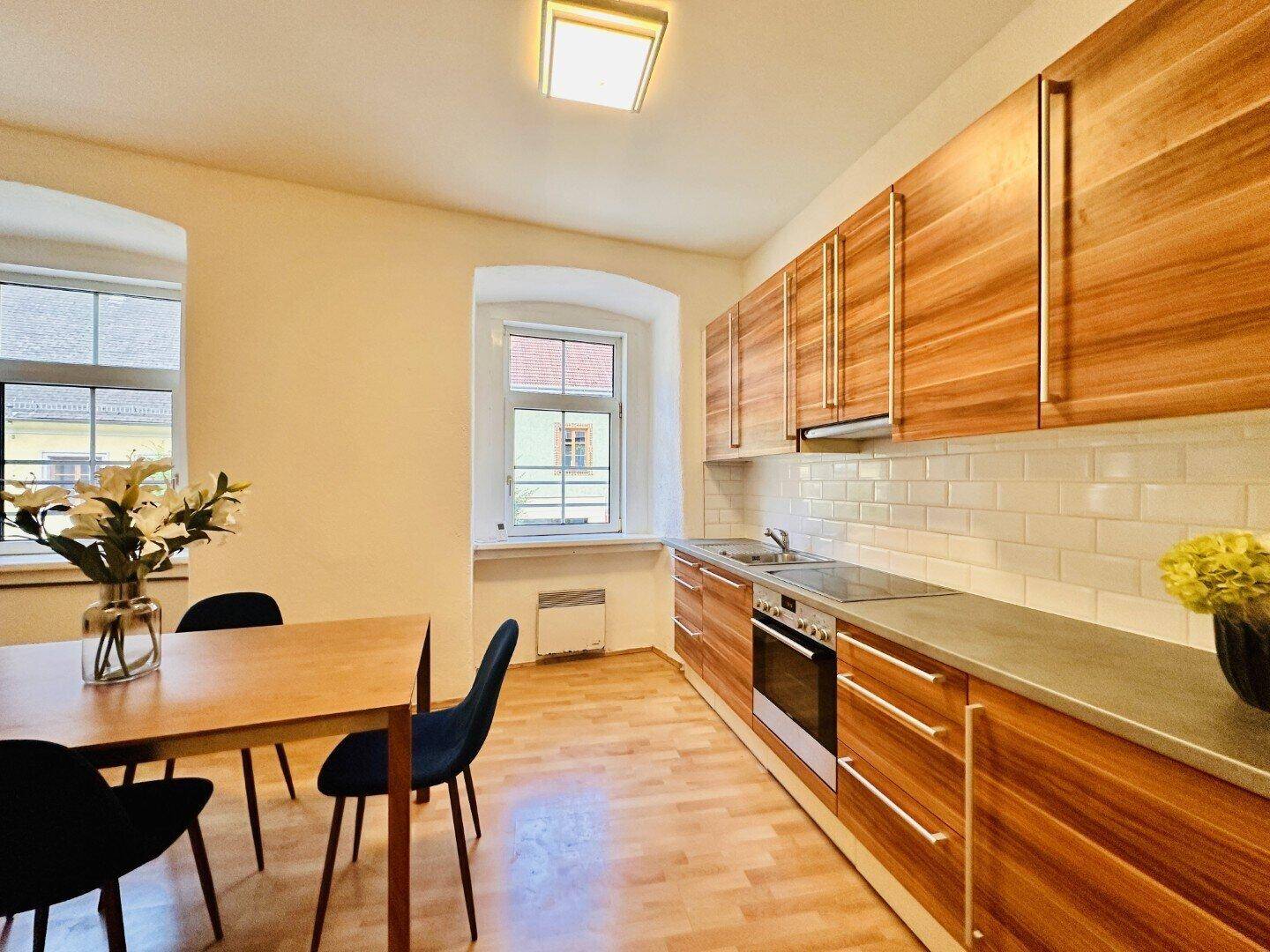 Detailansicht der modernen Küche mit Holzfronten, grauer Arbeitsplatte, Induktionskochfeld und Essbereich.
