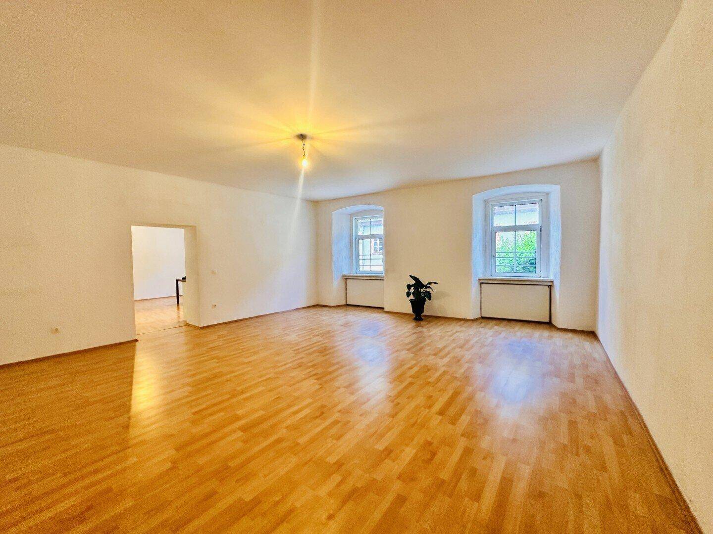 Heller, leerer Raum mit Holzboden, weißen Wänden und zwei Fenstern, bereit zur individuellen Gestaltung.