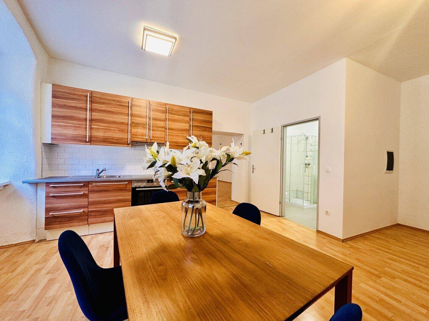 Wohnküche mit Essbereich und Holzschränken, angrenzend an ein Badezimmer mit Duschkabine.
