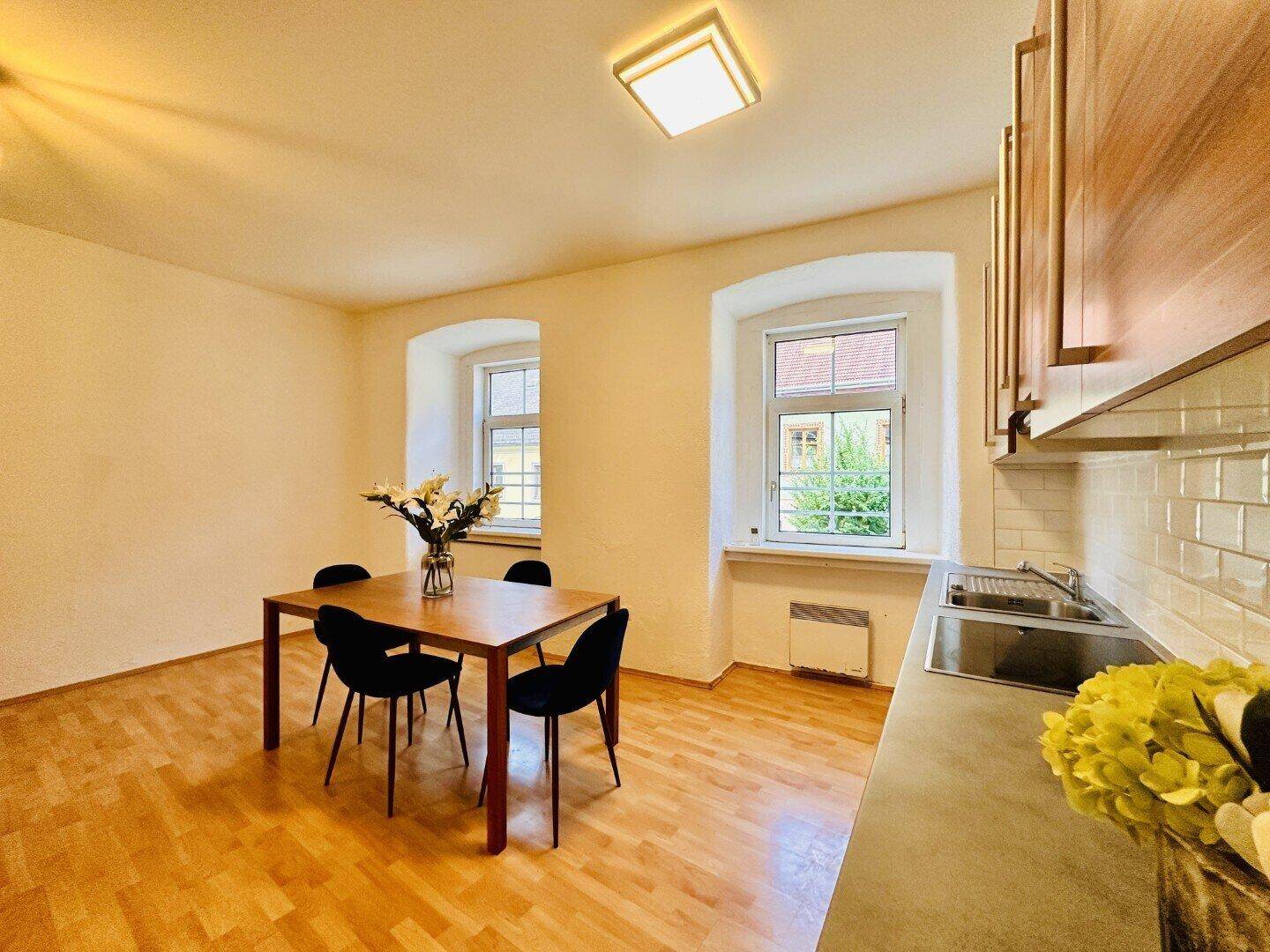 Helle Wohnküche mit Holzboden, modernen Holzschränken, Essbereich und Blick nach draußen.