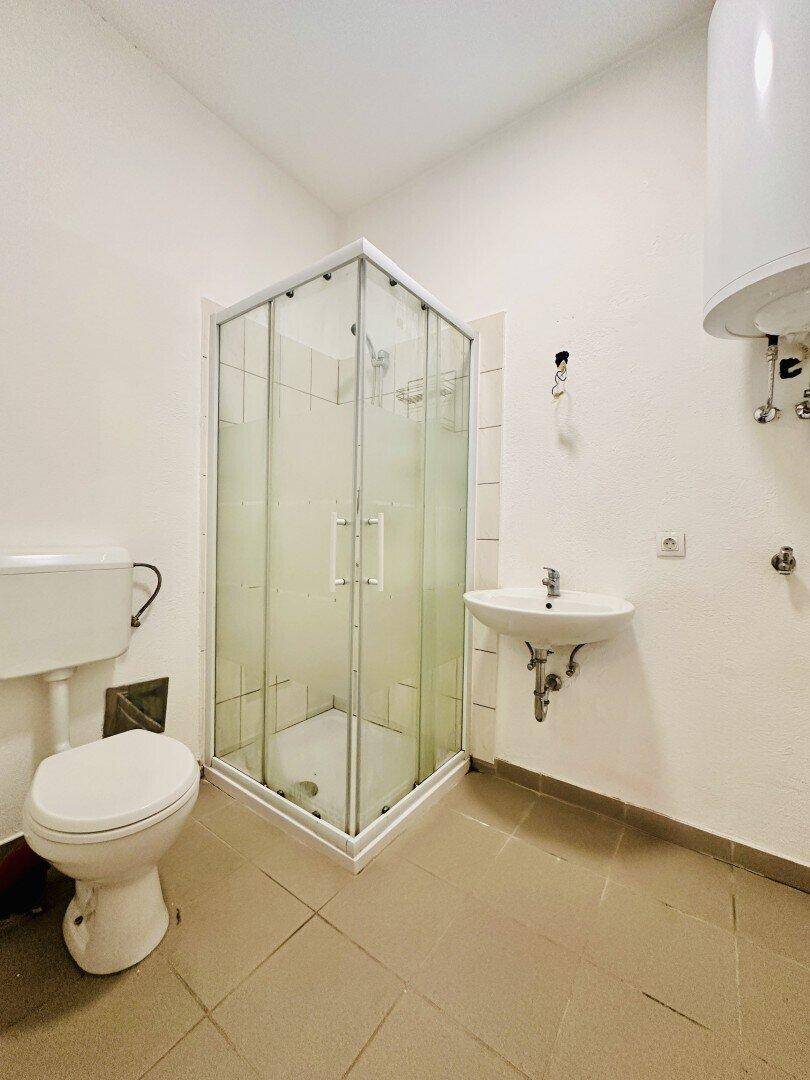 Funktionales Badezimmer mit Eckduschkabine, Toilette, Waschbecken und Warmwasserboiler.