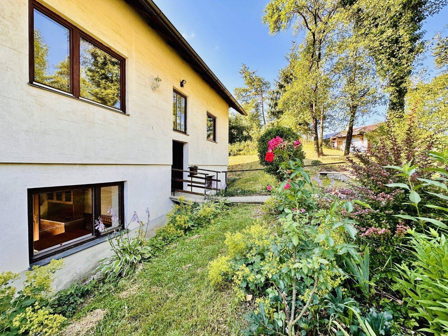 Seitenansicht des Hauses mit blühenden Pflanzen und Blick in den Garten.