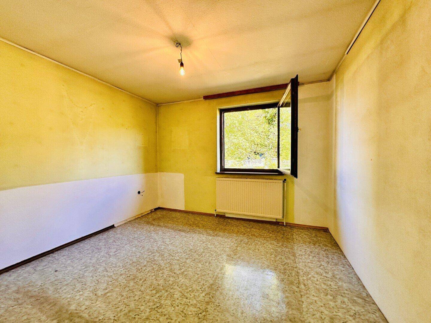 Helles Schlafzimmer mit gelben Wänden, Heizkörper und Blick ins Grüne.