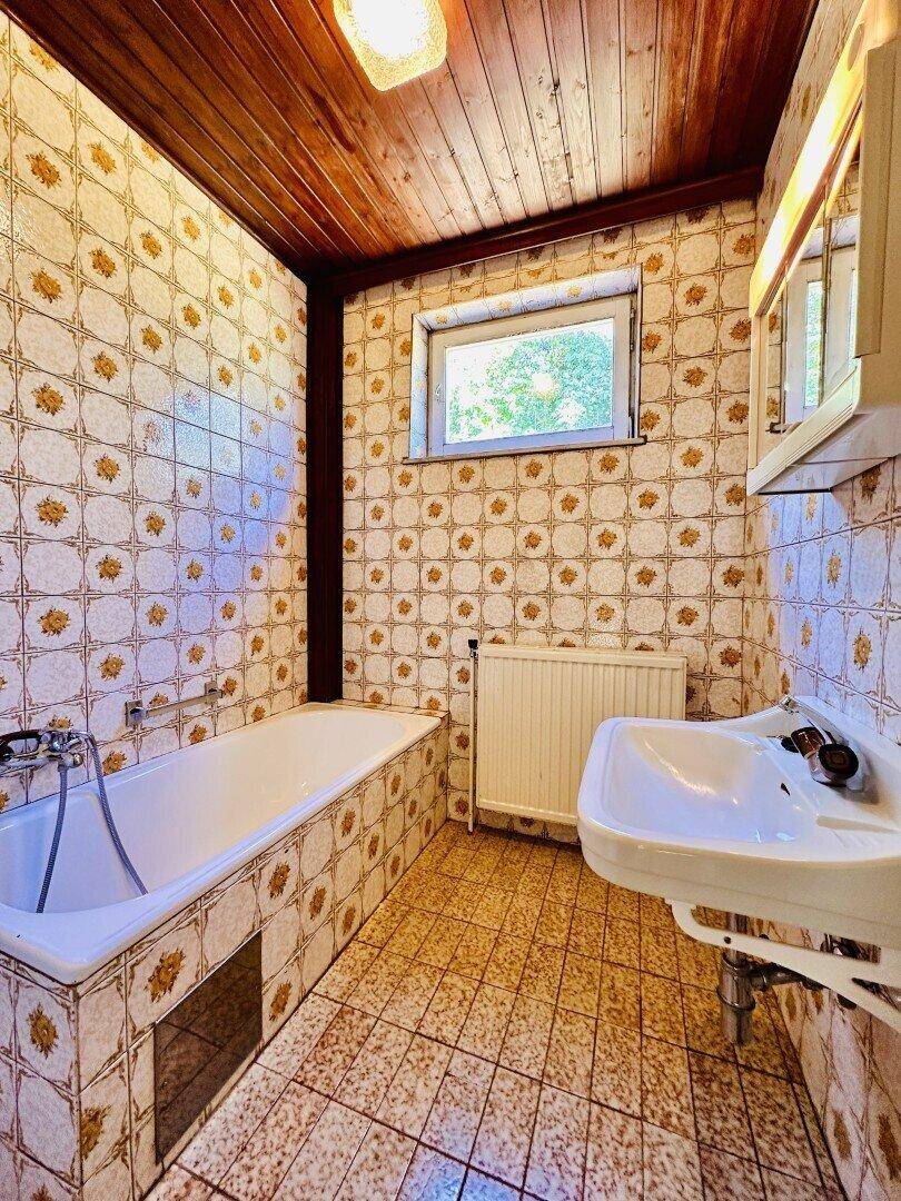 Badezimmer im 80er-Jahre-Stil mit gemusterten Fliesen, Badewanne und Waschbecken.