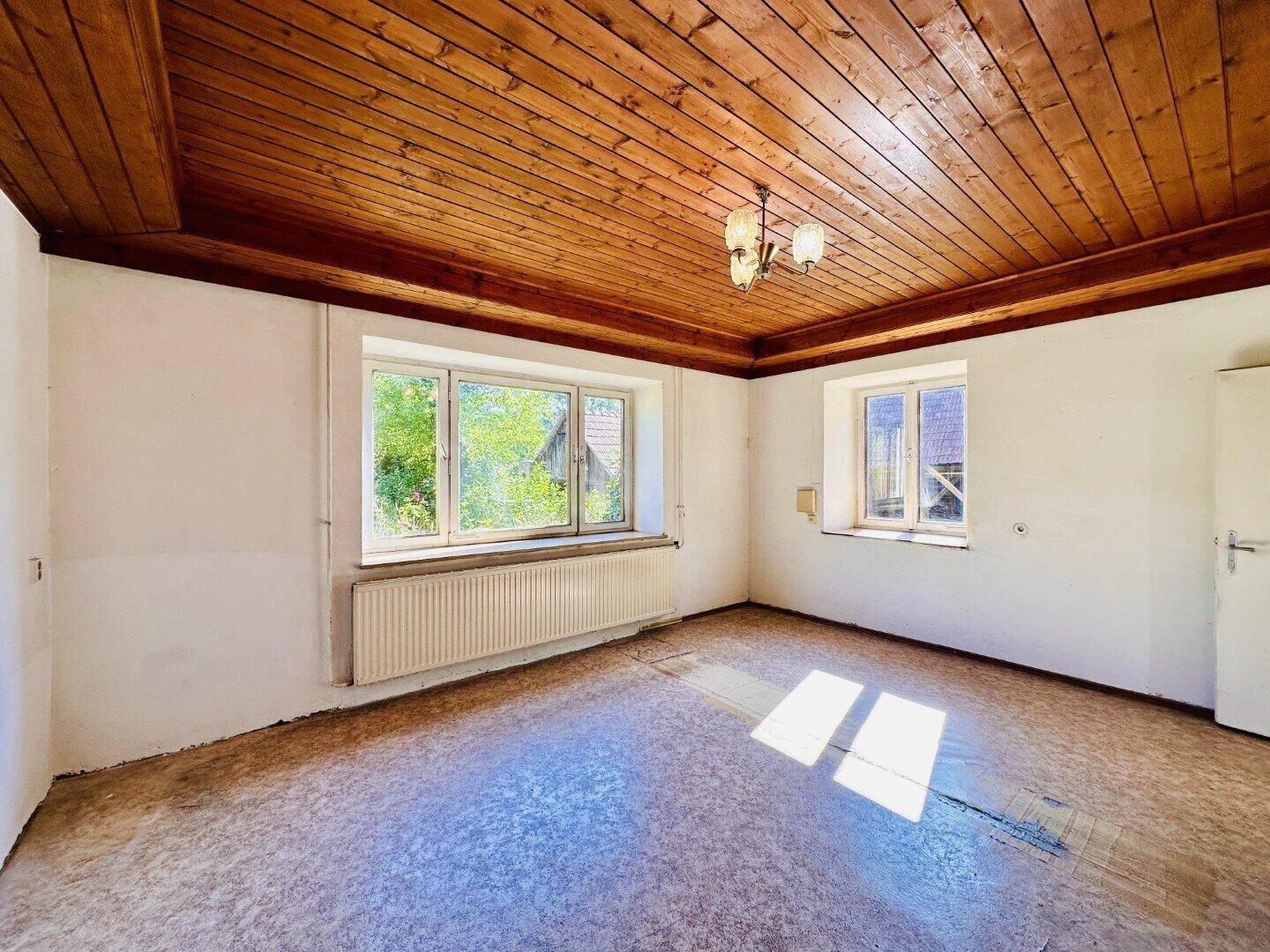 Helles Zimmer mit Holzbalkendecke, großen Fenstern und Blick auf die umliegende Natur.
