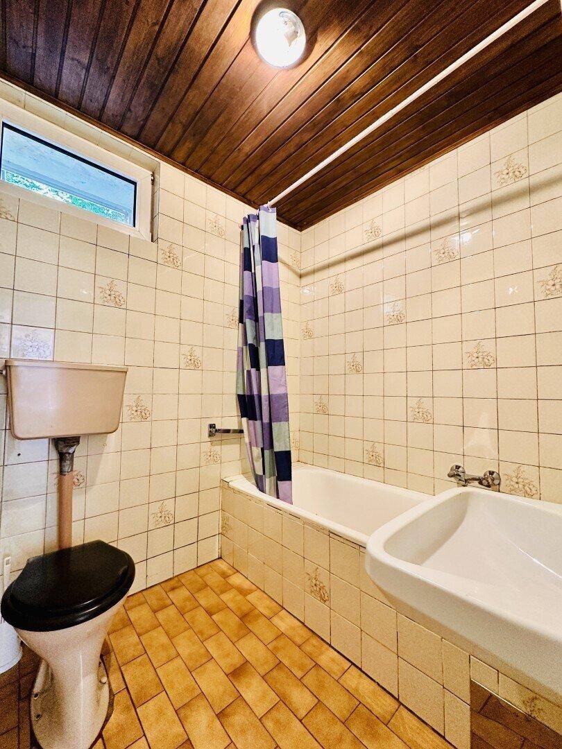 Badezimmer im 80er-Jahre-Stil mit gemusterten Fliesen, Badewanne und Toilette.