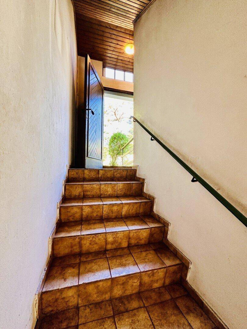 Geflieste Treppe mit Holzgeländer führt zum Eingangsbereich des Hauses.