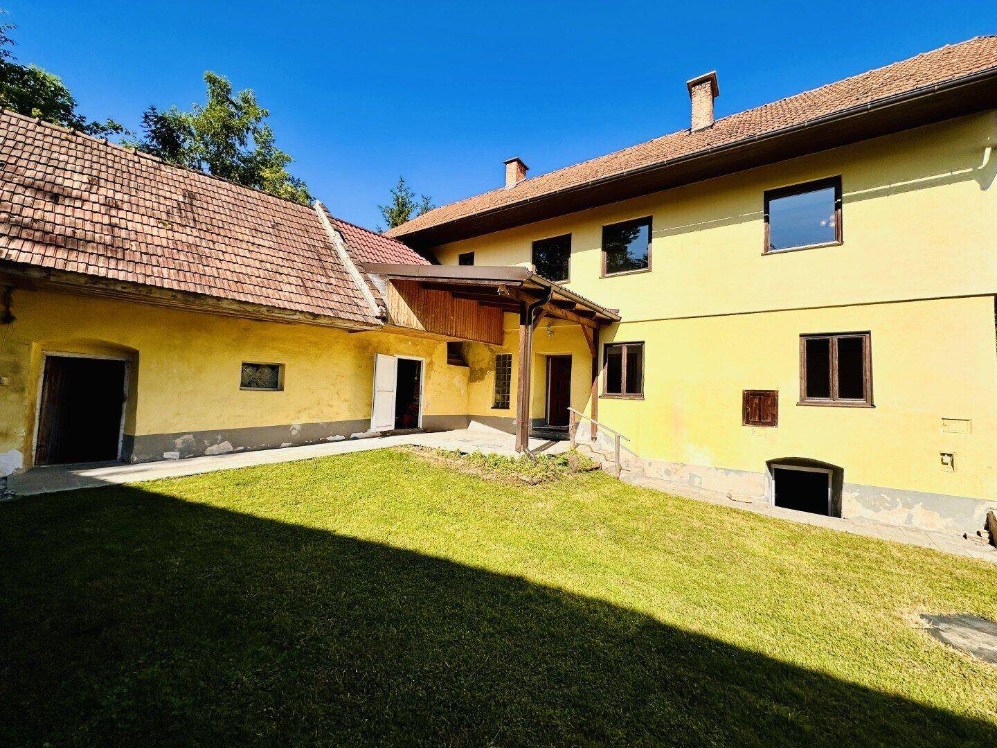 Rückseite des gelben Hauses mit großem Rasenbereich und angrenzenden Nebengebäuden.