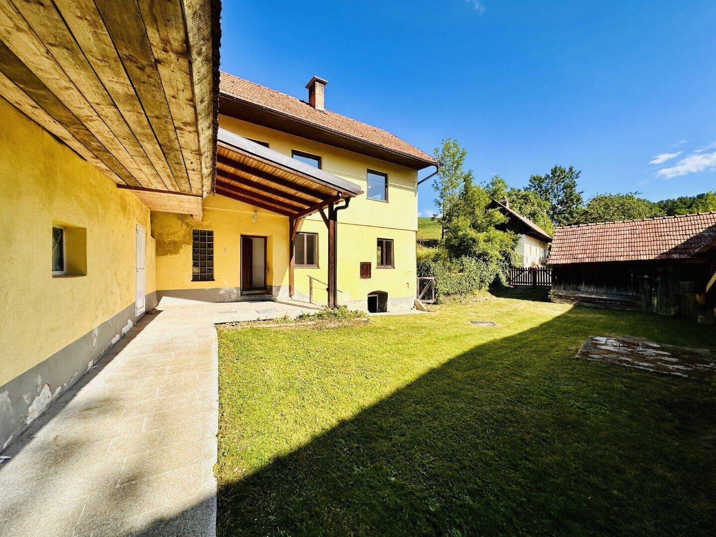 Seitenansicht des gelben Hauses mit gepflegtem Rasen und Nebengebäuden im Hintergrund.