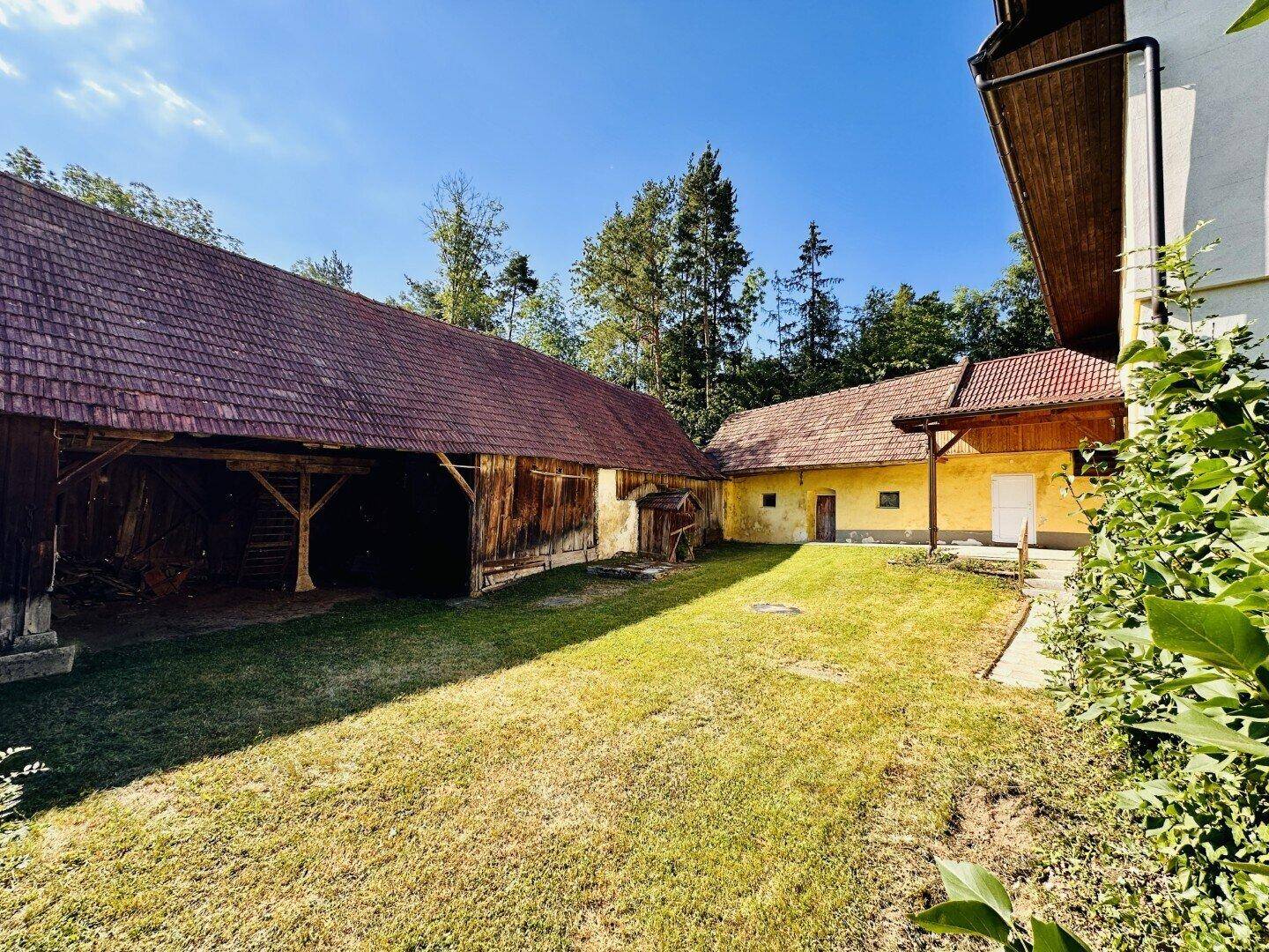 Großer grüner Gartenbereich mit alten Scheunen und Nebengebäuden unter blauem Himmel.