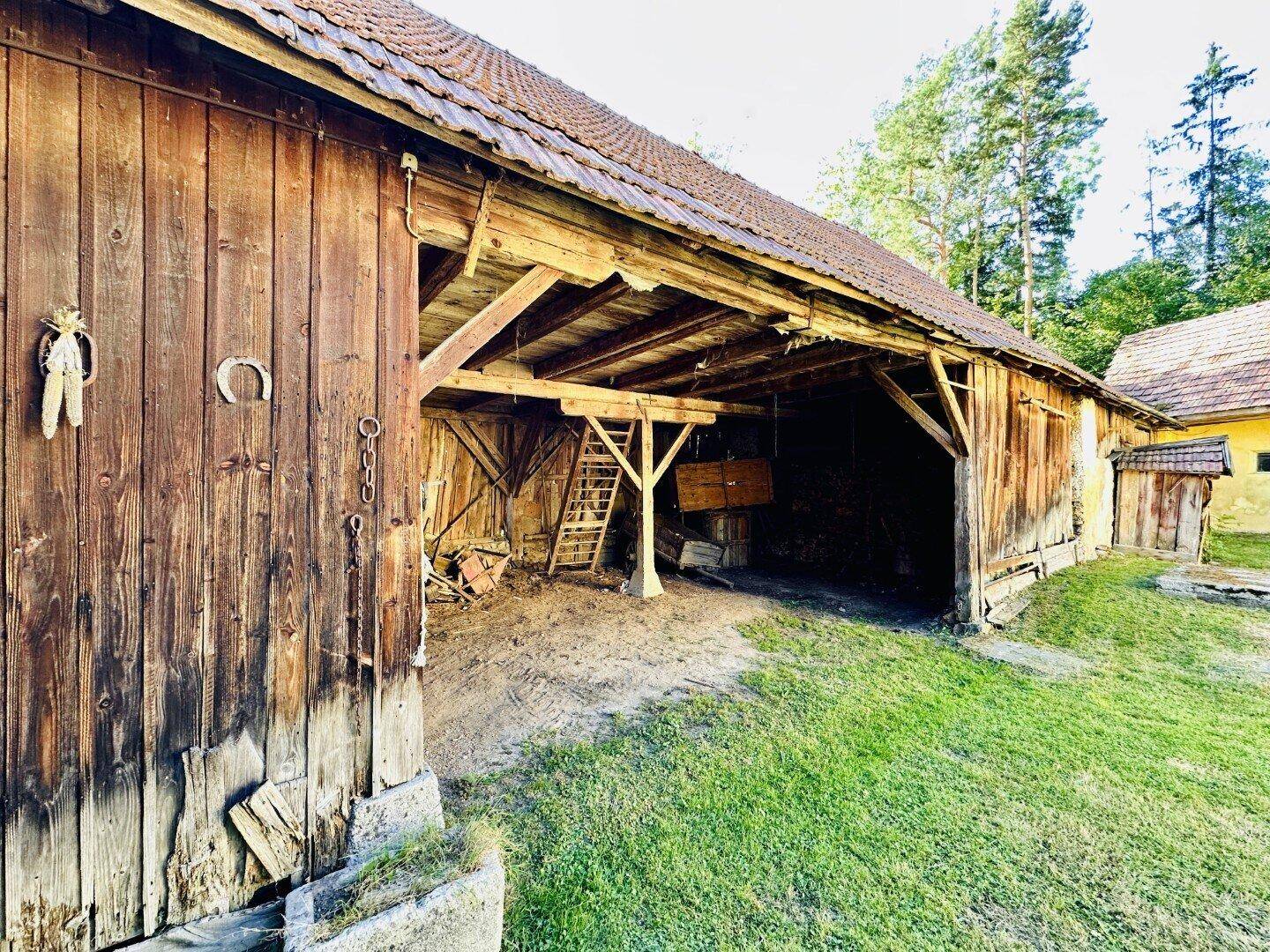 Alte Holzscheune mit offenem Eingang und rustikalem Charme in ländlicher Umgebung.