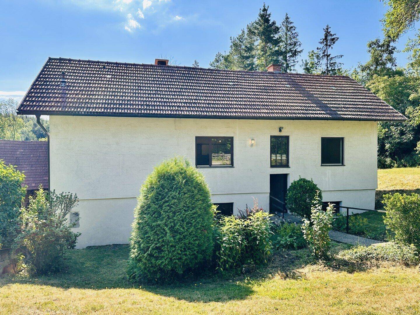 Vorderansicht eines Einfamilienhauses mit weißer Fassade, Ziegeldach und gepflegter Bepflanzung.
