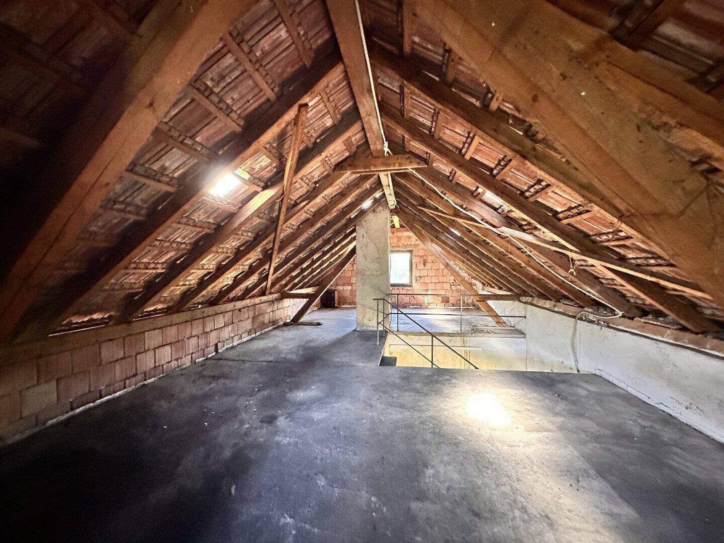 Geräumiger Dachboden mit sichtbaren Holzbalken und Dachziegeln, bereit für den Ausbau.