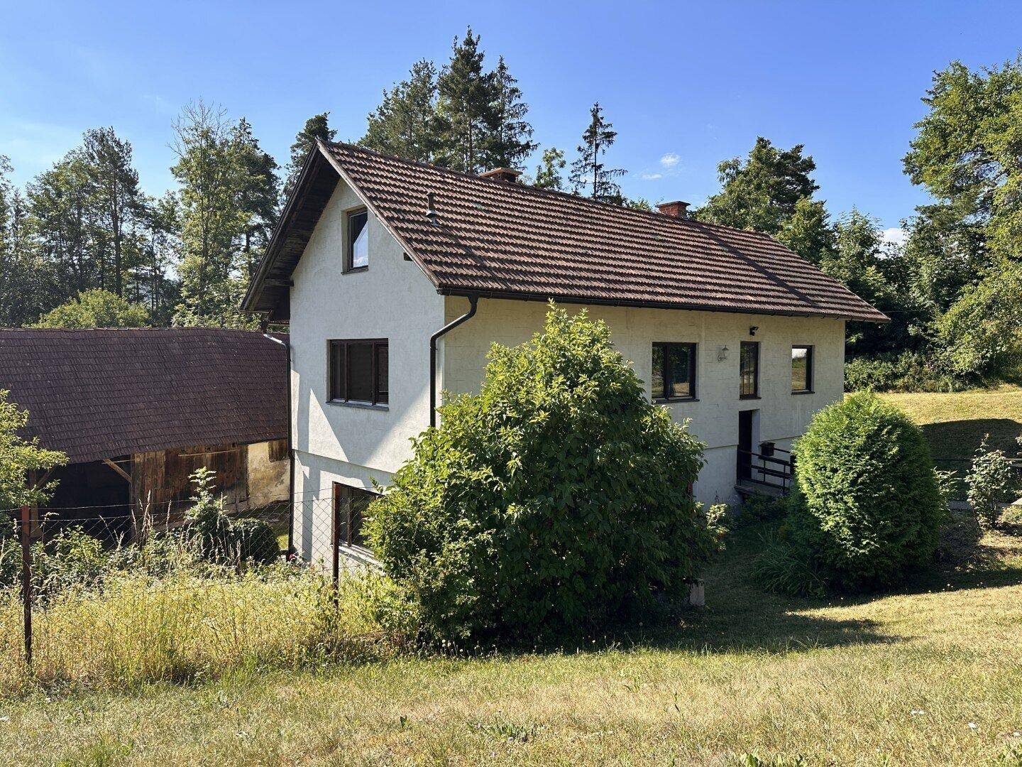 Freistehendes Haus mit weißer Fassade und Ziegeldach, umgeben von weitläufigen Grünflächen und Bäumen.