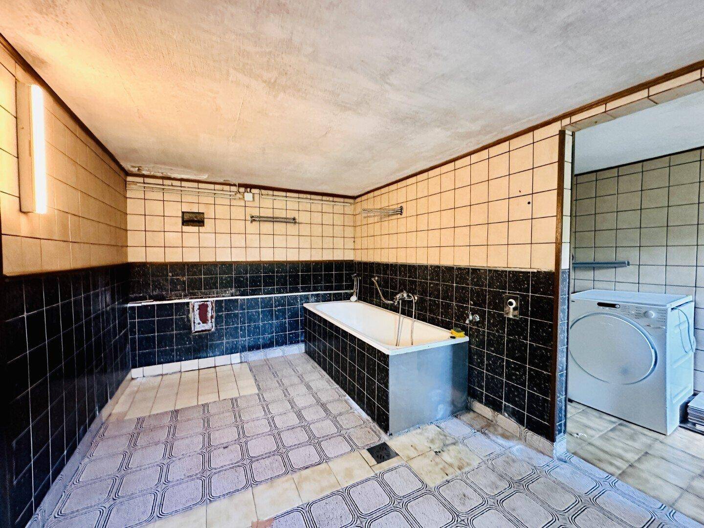Großes Badezimmer im Keller mit Fliesen, Badewanne und Waschmaschine.
