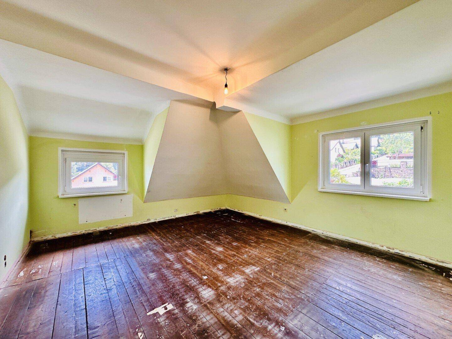 Schlafzimmer im Dachgeschoss mit schrägen Wänden, grün gestrichenen Wänden und Holzboden.