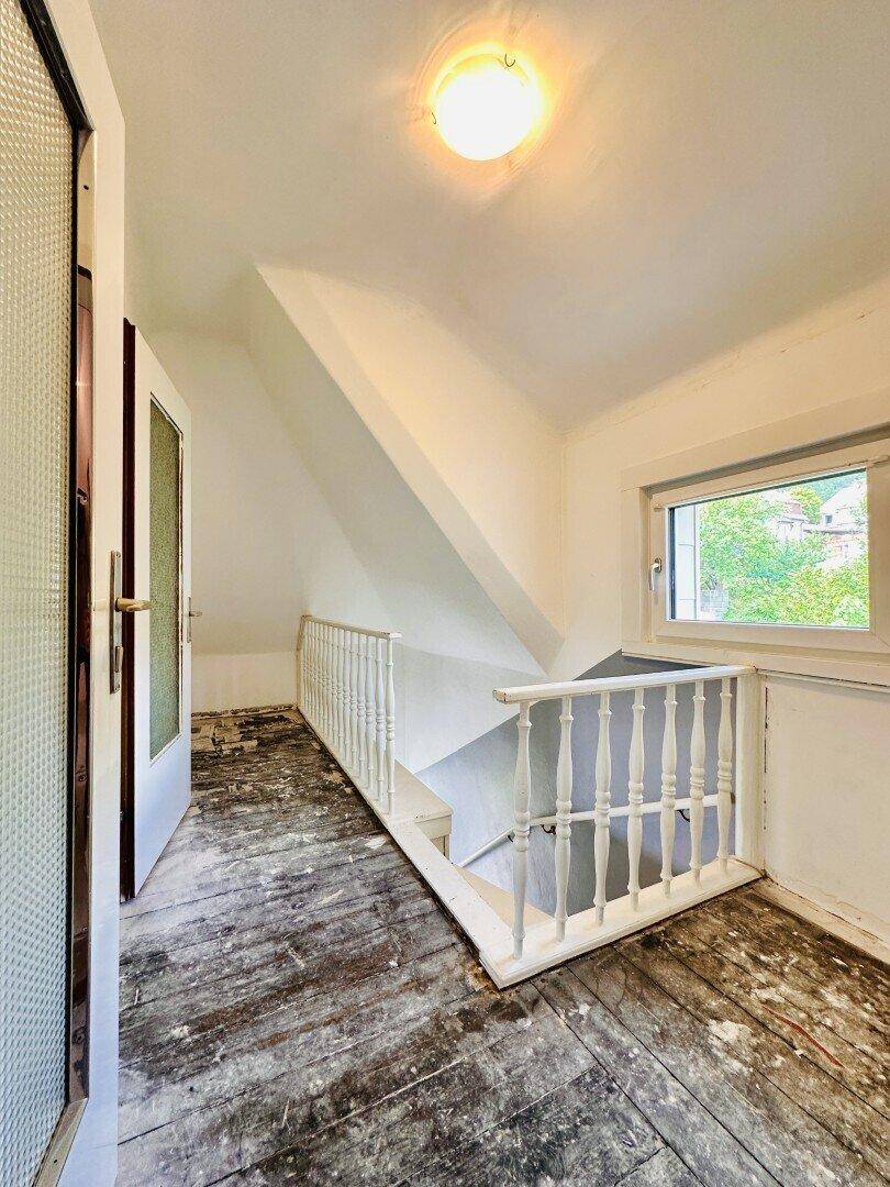 Dachgeschossflur mit Holztreppe, weißem Geländer und Fenster mit Blick ins Grüne.