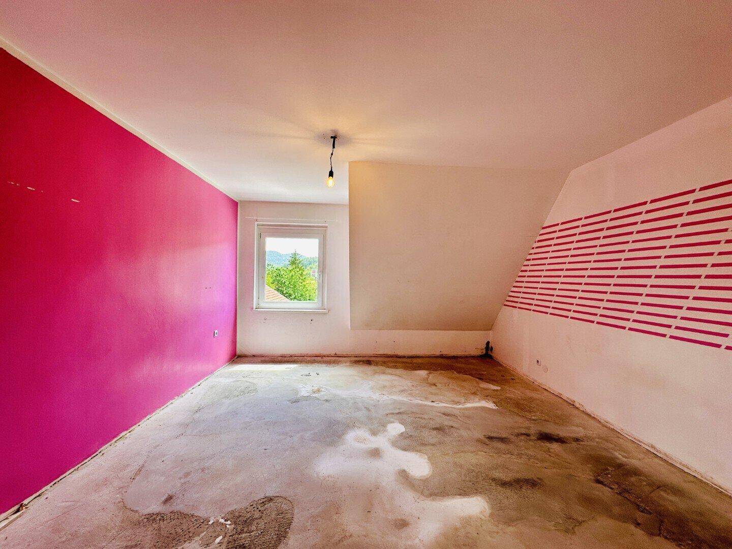 Schlafzimmer im Dachgeschoss mit schrägen Wänden, pinker Akzentwand und Betonboden.