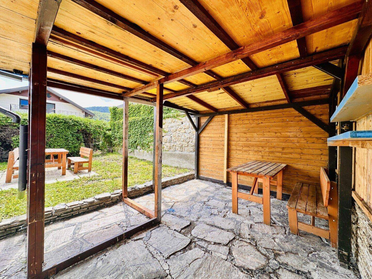 Überdachter Sitzbereich im Freien mit Holztisch und Bänken, ideal für Entspannung.