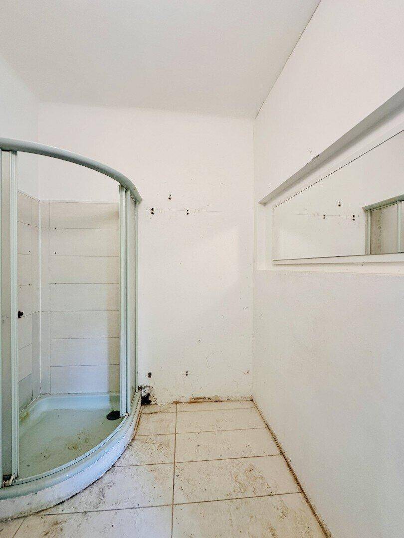 Badezimmer mit alter Duschkabine, hellen Fliesen und Renovierungsbedarf.