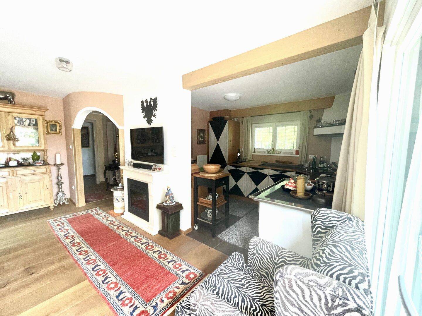 Offener Wohnbereich mit Kamin, Holzboden und Blick in die angrenzende Küche mit Zebra-Sessel.