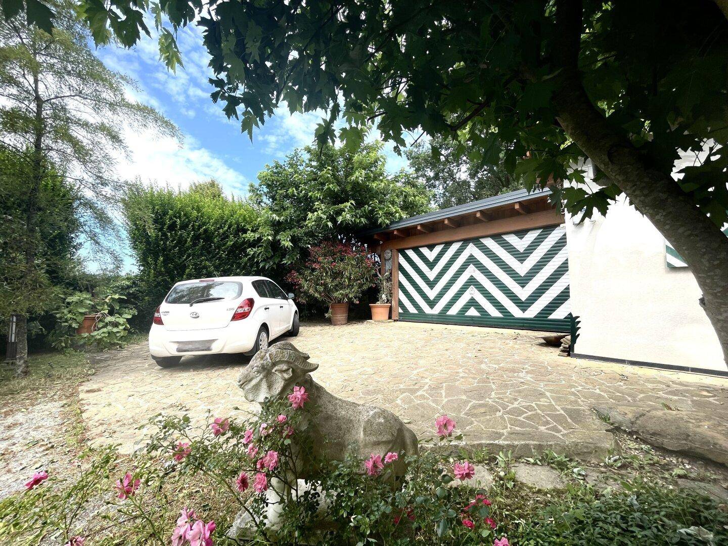 Parkplatz mit Natursteinpflaster vor einer Garage mit markantem grün-weißem Muster und Gartenblick.