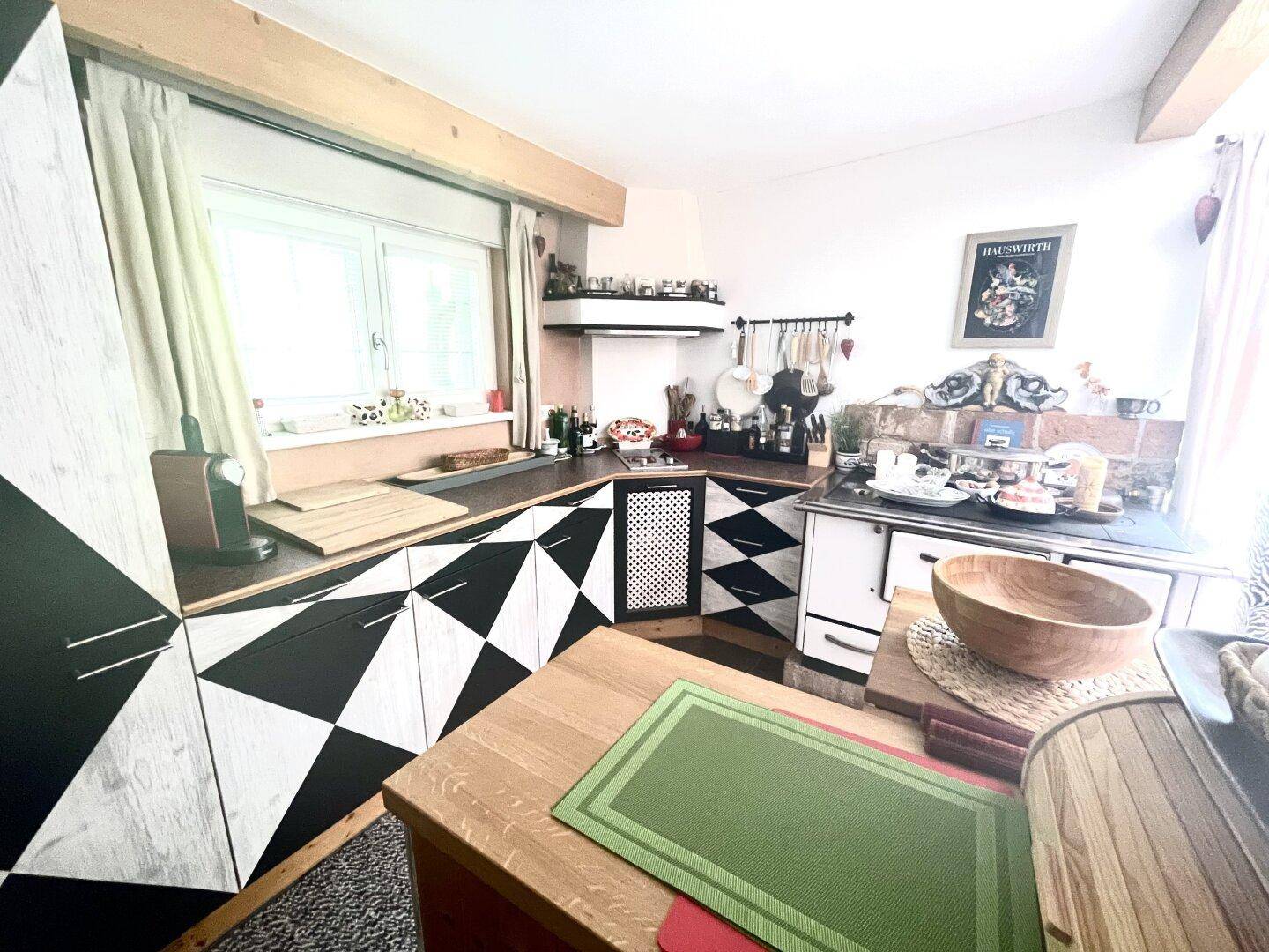 Gemütliche Küche mit markanten schwarz-weißen Fronten, traditionellem Holzherd und viel Tageslicht.