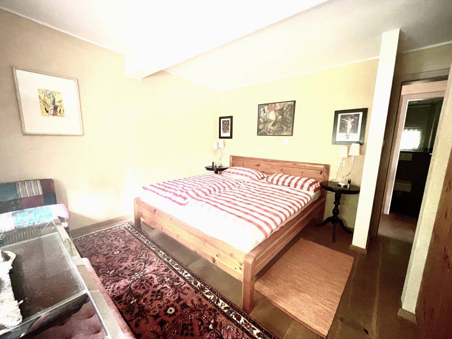 Gemütliches Schlafzimmer mit Holzbett, gestreifter Bettwäsche und Teppichen auf dem Boden.