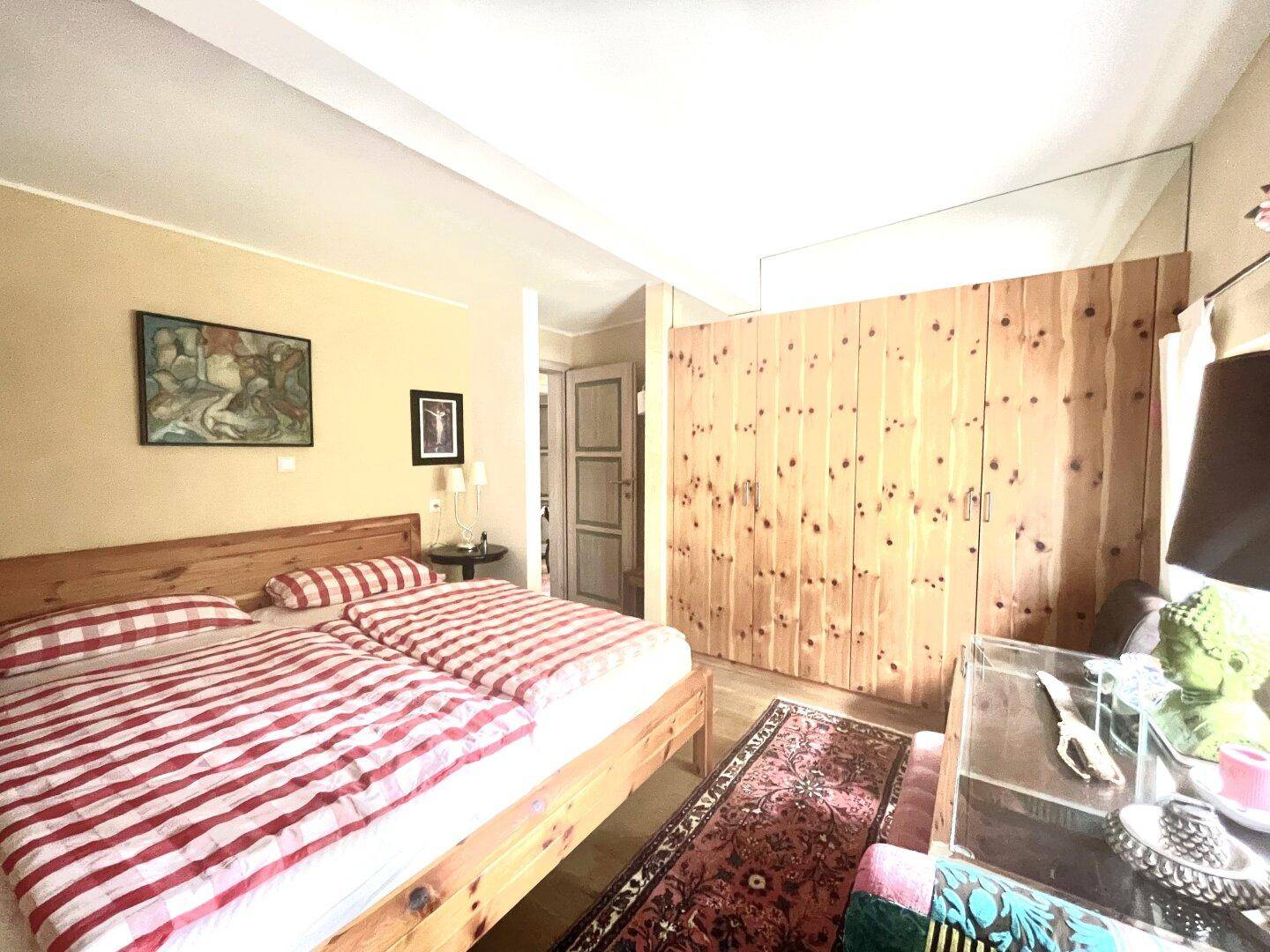 Helles Schlafzimmer mit Holzbett, Holzschrank und rot-weiß gestreifter Bettwäsche.