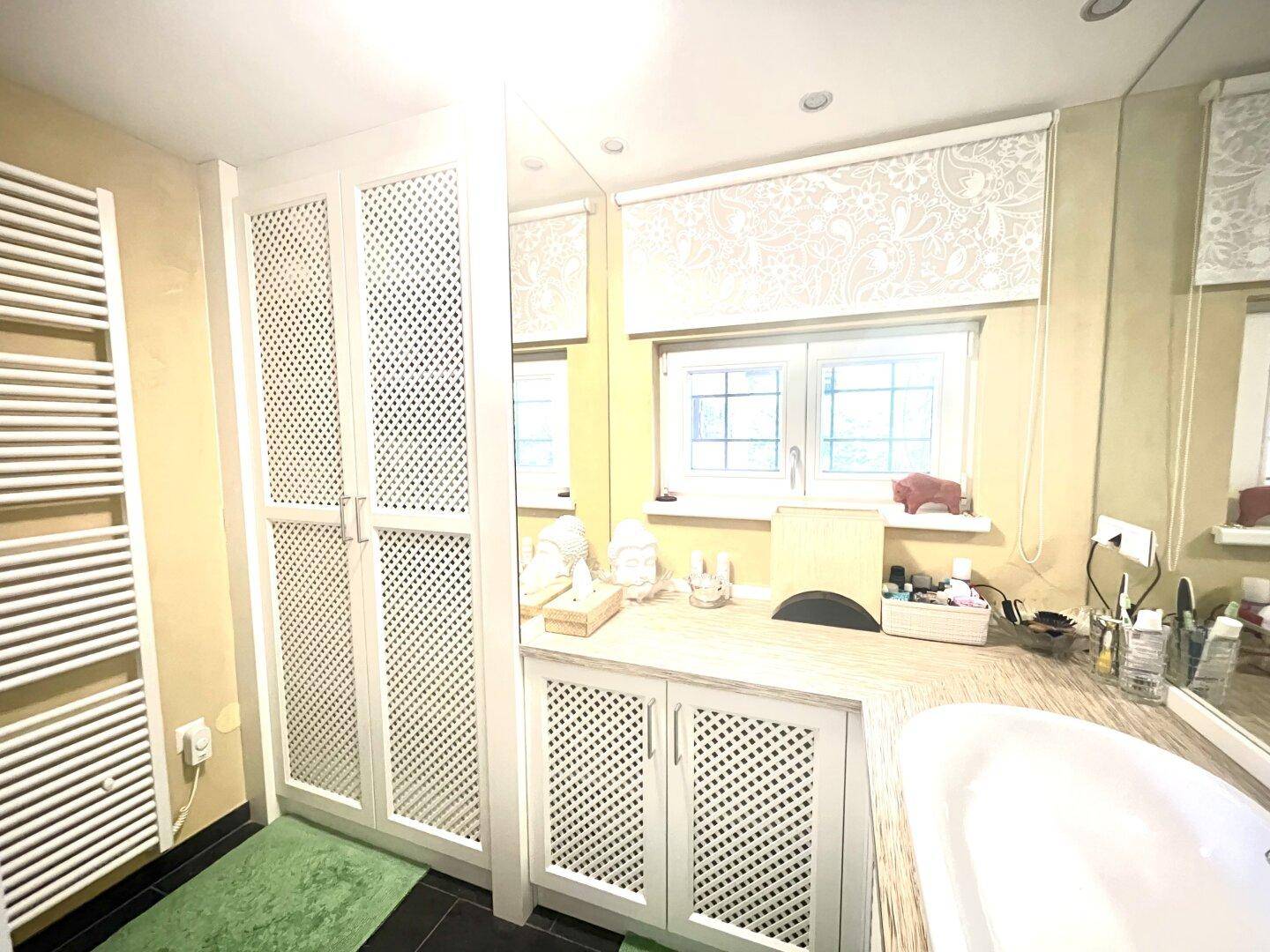 Helles Badezimmer mit Fenster, Waschtisch und integrierten Schränken, sowie einem Handtuchheizkörper.