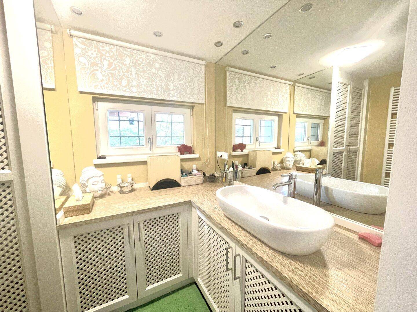 Modernes Badezimmer mit ovalem Aufsatzwaschbecken, großem Spiegel und integrierten Schränken.