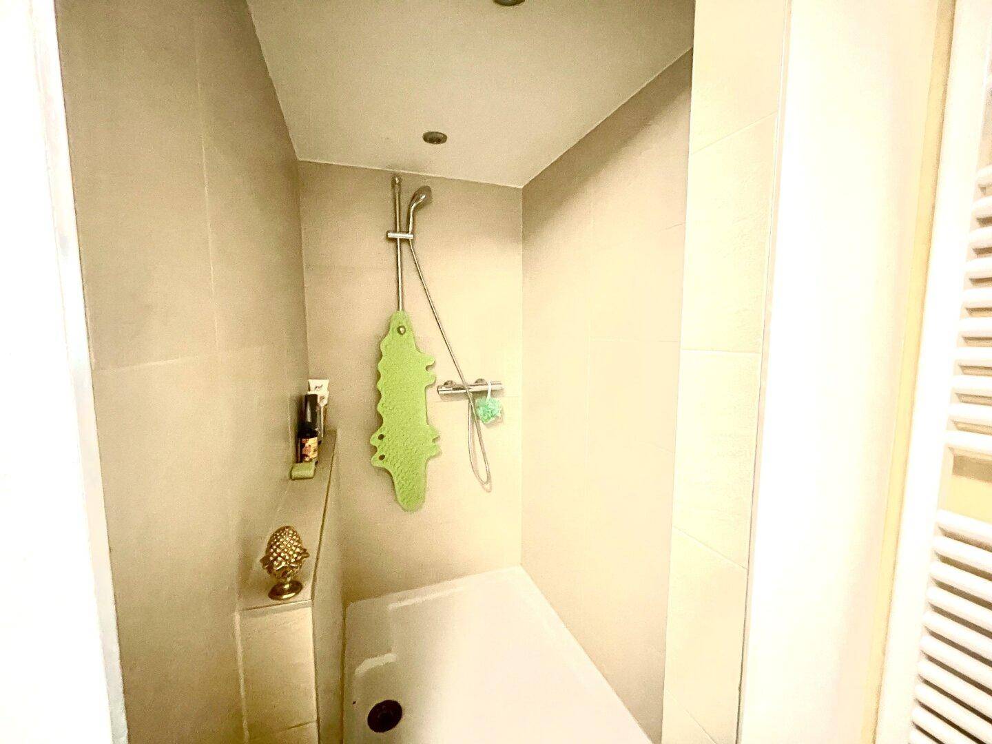 Duschbereich mit Badewanne und beigefarbenen Fliesen, sowie einer Duscharmatur.