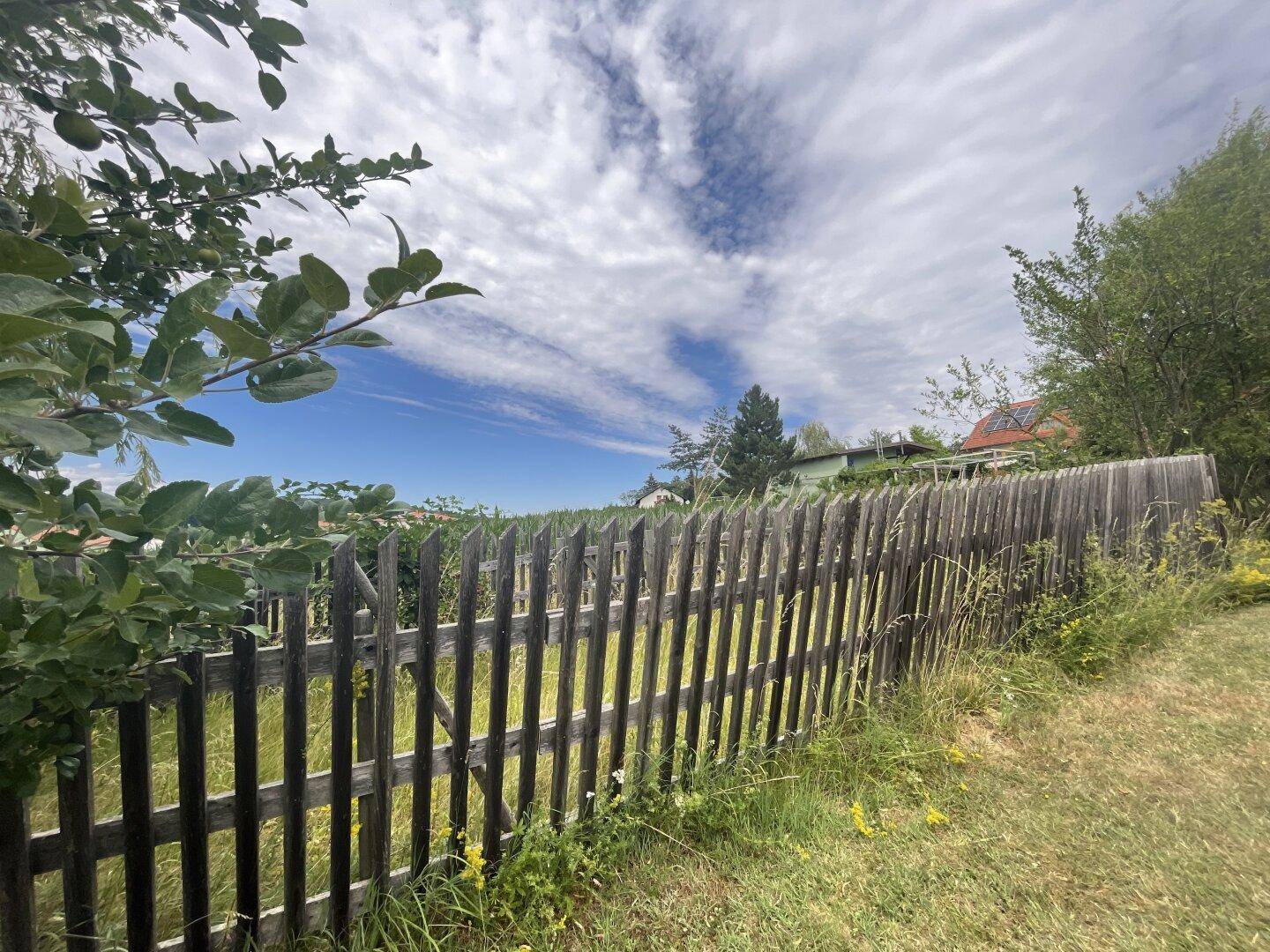 Rustikaler Holzzaun umgeben von Gras und Bäumen unter einem weiten Himmel.