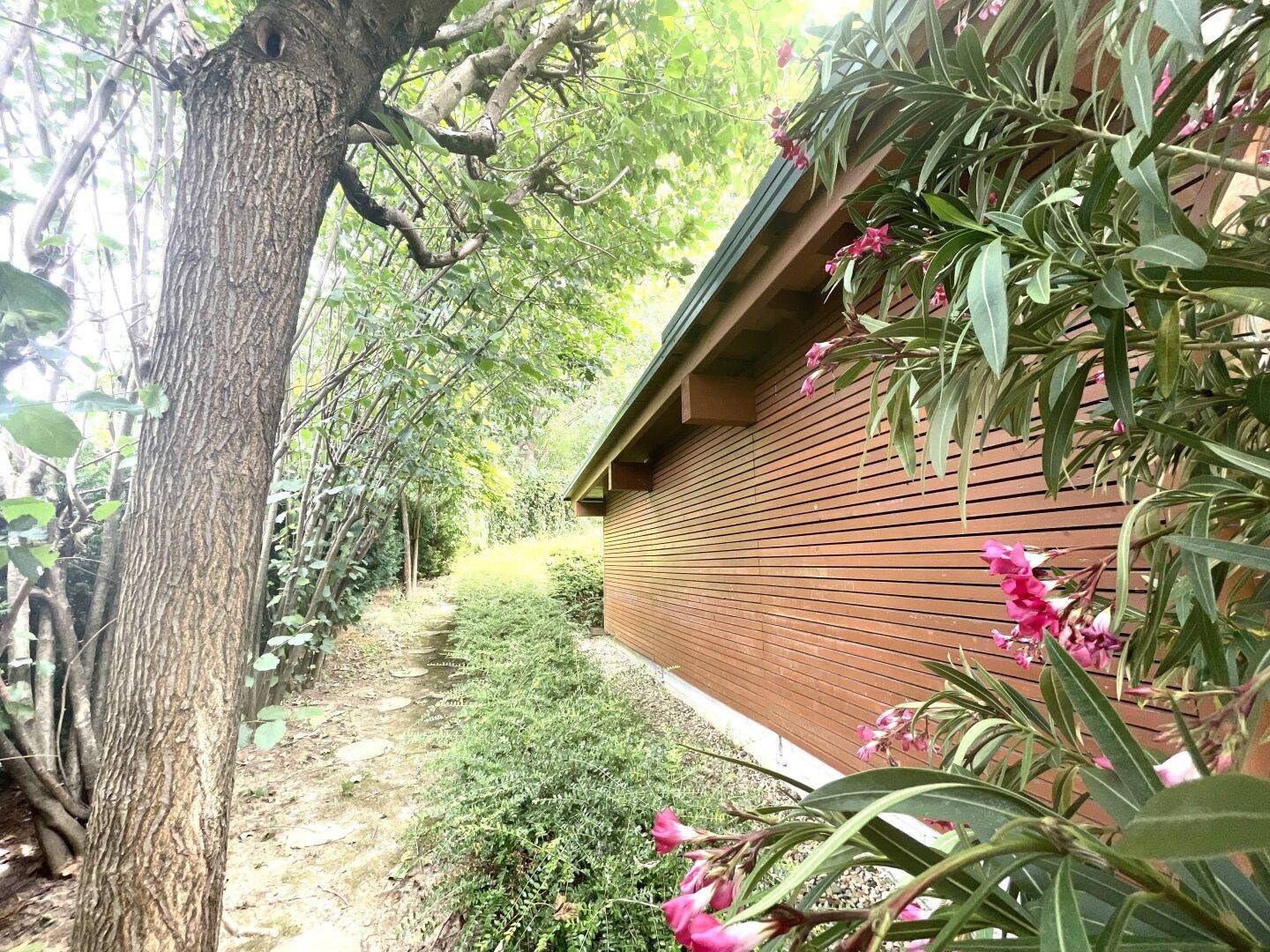 Holzfassade eines Gebäudes mit blühenden Pflanzen und einem Baum im Vordergrund.