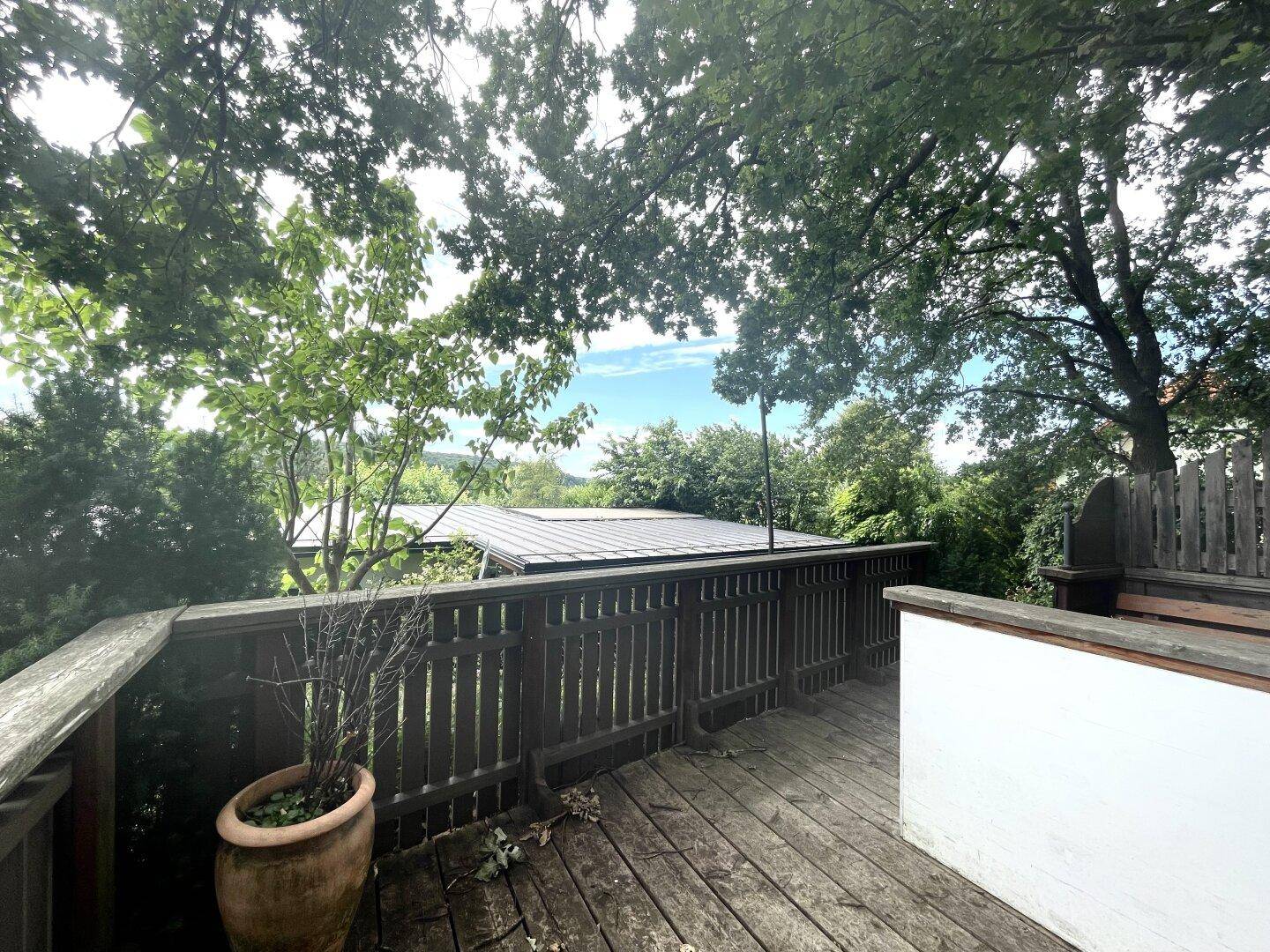 Hölzerner Balkon mit Geländer und Blick auf die grüne Umgebung und Dächer.