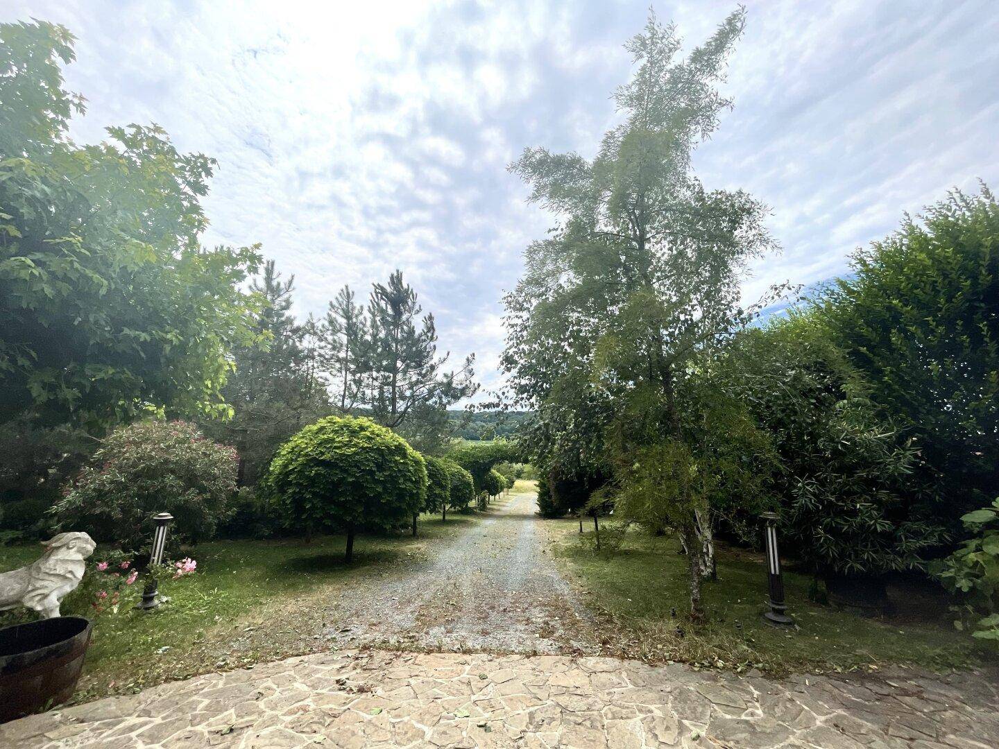Kiesauffahrt gesäumt von Bäumen, mit einem Steinplattenweg im Vordergrund.