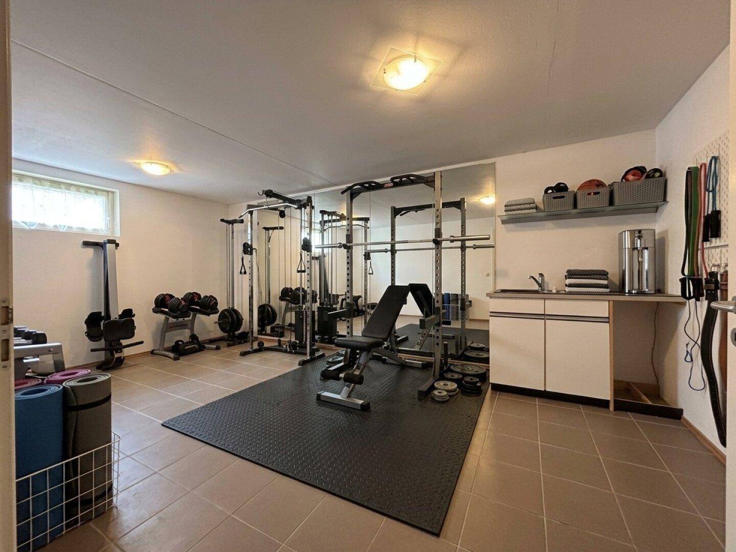 Gut ausgestatteter Fitnessraum im Untergeschoss mit verschiedenen Trainingsgeräten und Spiegelfläche.
