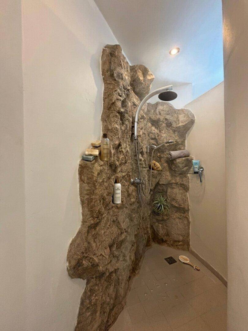 Einzigartige Dusche mit Natursteinwand und Regenduschkopf.