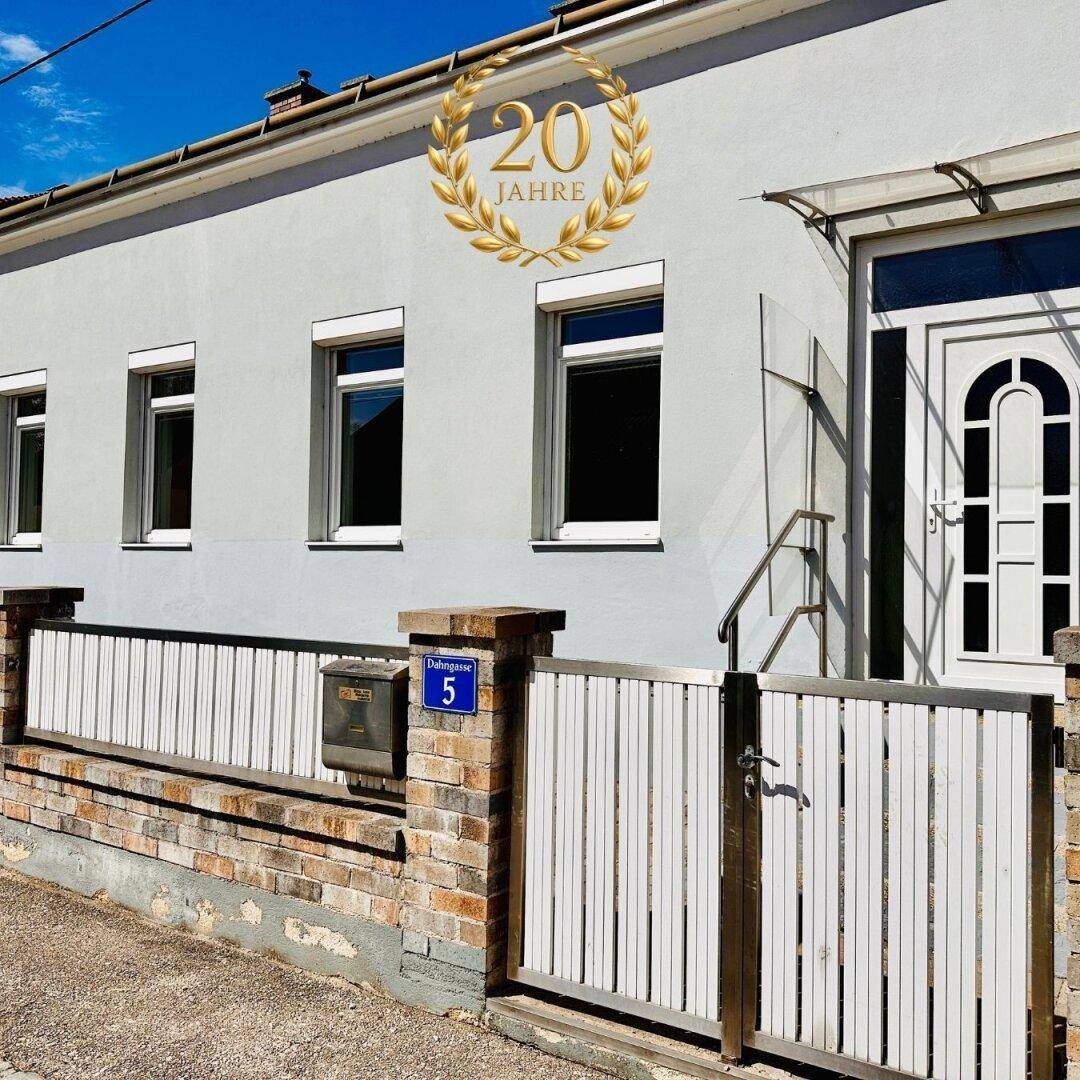 Fassade eines Einfamilienhauses mit weißer Eingangstür und einem "20 Jahre" Jubiläumslogo.