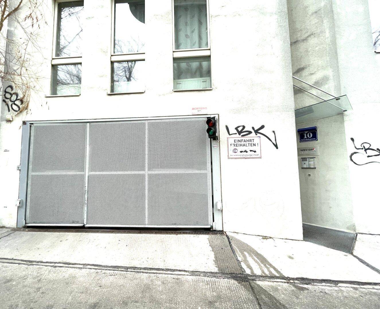Eingang zu einer Tiefgarage mit Metalltor und Hinweisschildern an der Fassade.