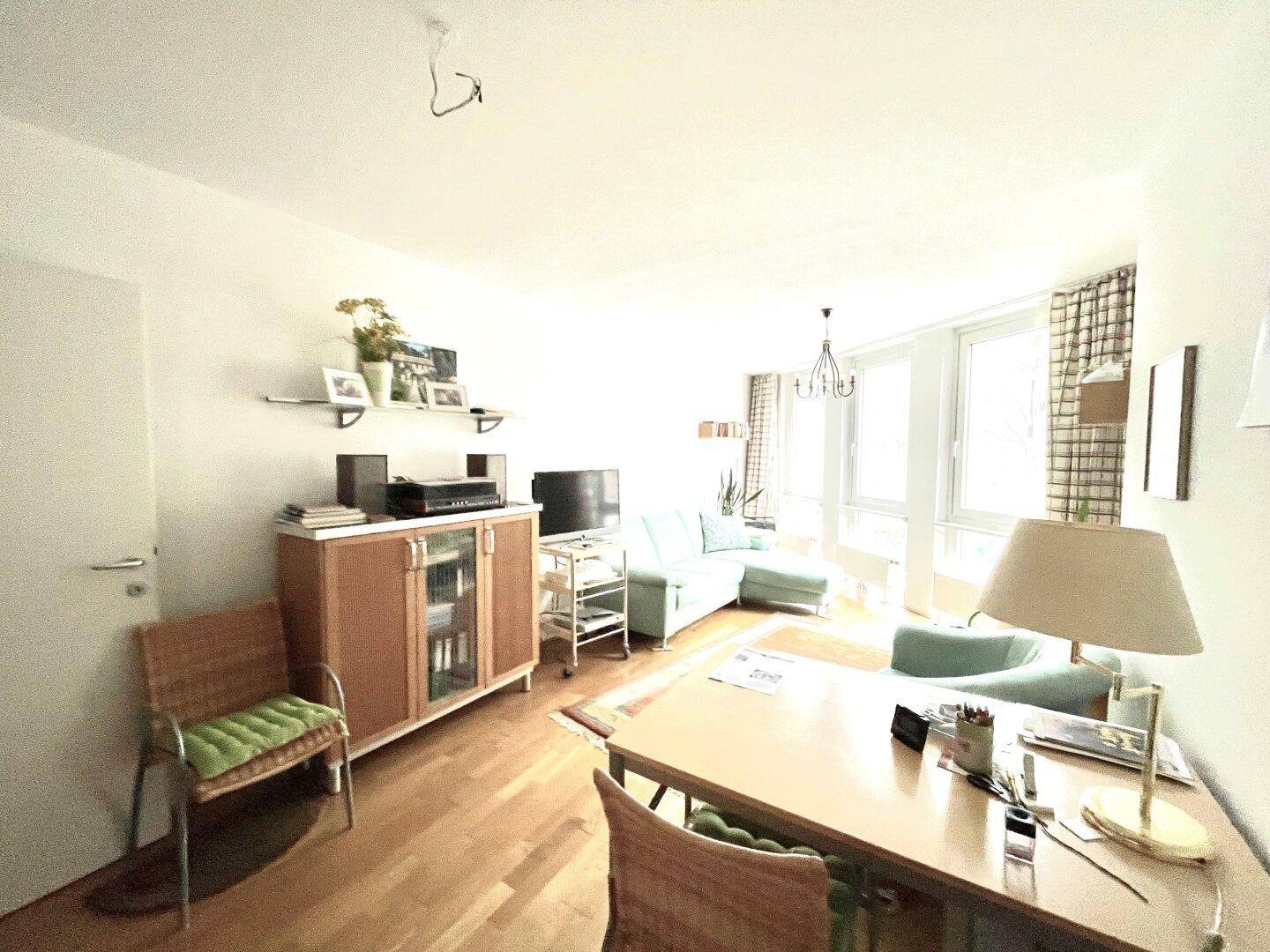 Helles Wohnzimmer mit Holzboden, Sofa und einem Schreibtischbereich am Fenster.