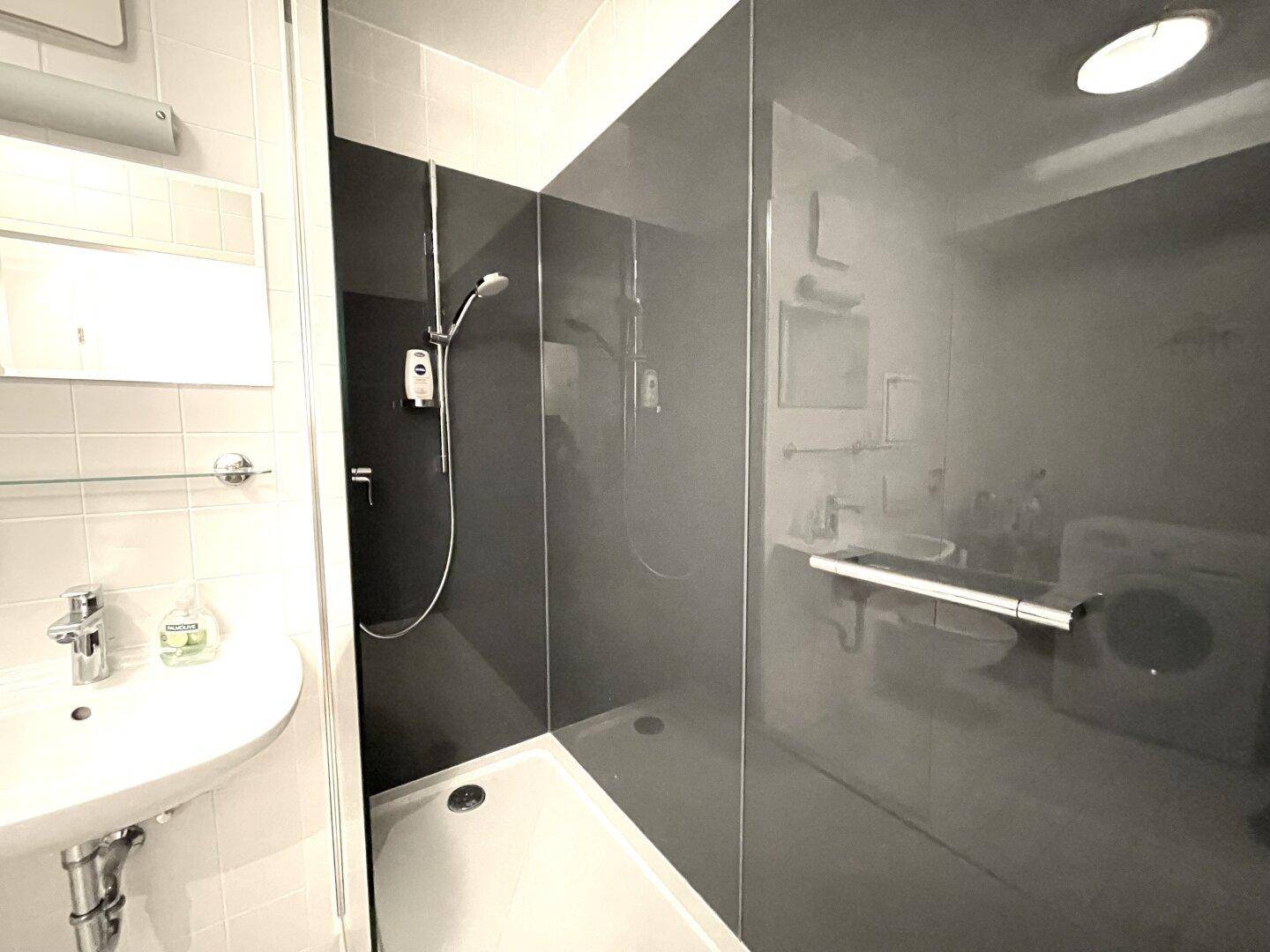 Modernes Badezimmer mit Dusche, Waschbecken und dunklen Wandpaneelen.