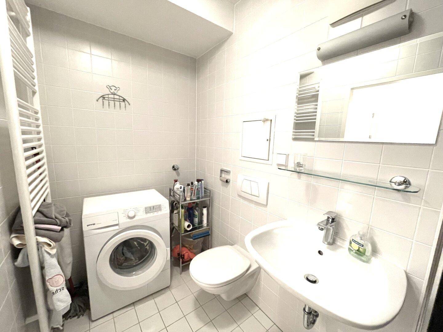 Funktionales Badezimmer mit Waschmaschine, WC, Waschbecken und Handtuchheizkörper.