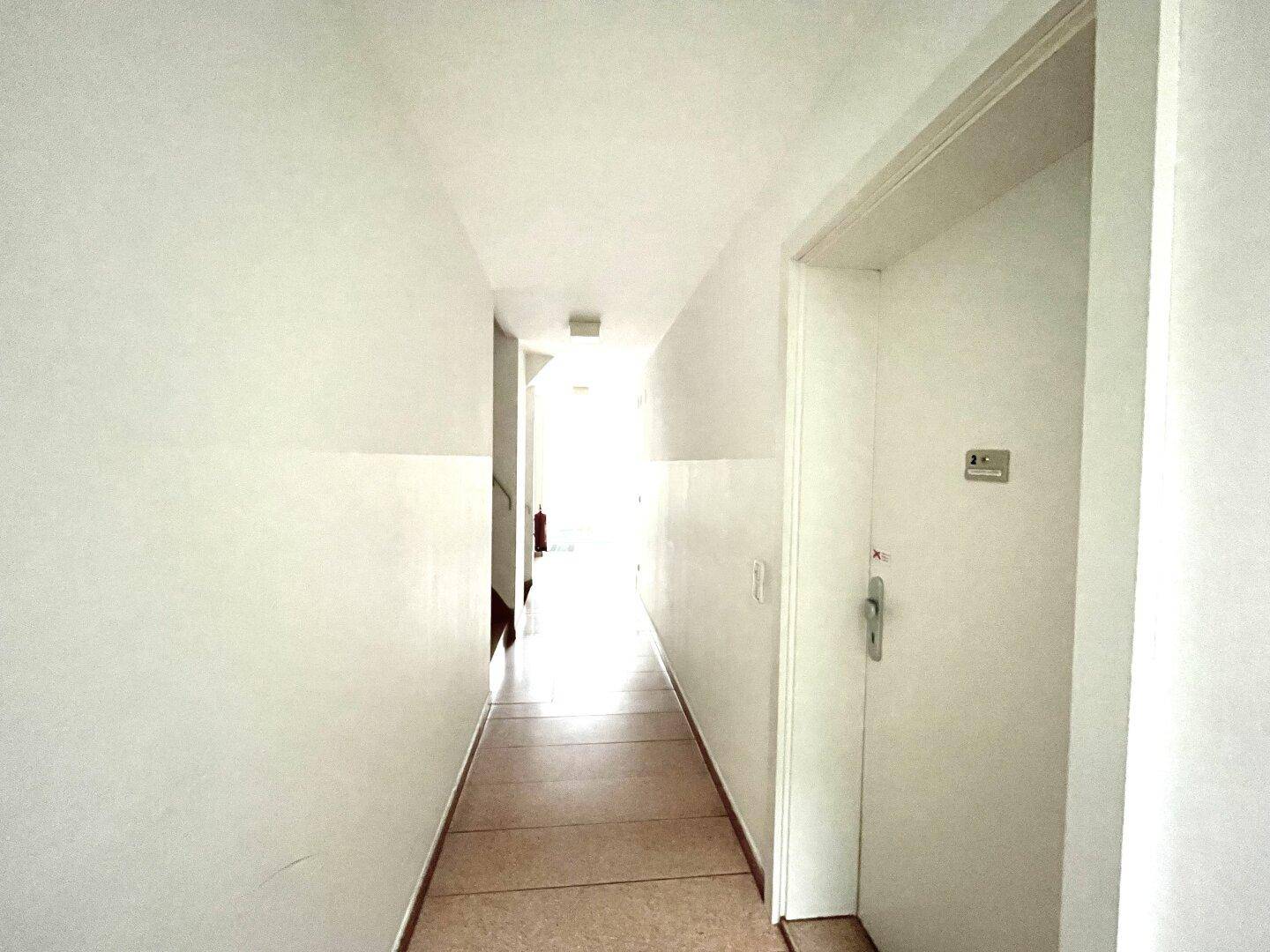 Heller Flur mit weiß gestrichenen Wänden und Fliesenboden, der in die Ferne führt.