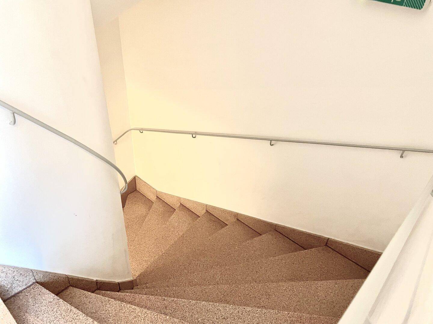 Wendeltreppe mit Steinstufen und Metallhandlauf in einem hellen Treppenhaus.