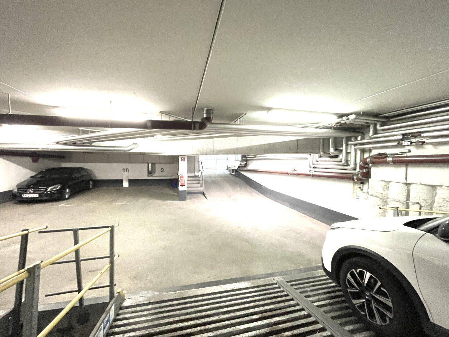 Geräumige Tiefgarage mit mehreren Stellplätzen und sichtbaren Installationen an der Decke.